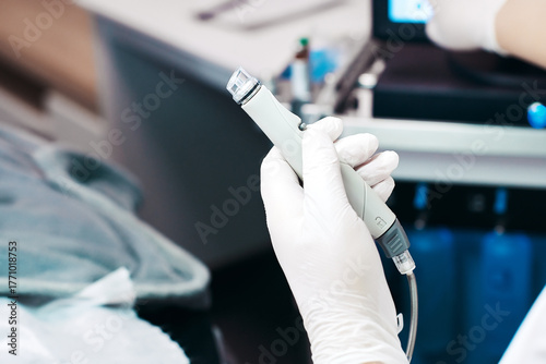 Medical professional holding a microneedling device in a clinical setting with equipment visible