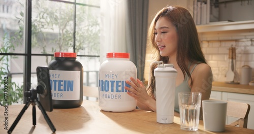 Young Asian female health influencer live streaming on social media sharing nutrition tips with whey protein powder by smartphone. Healthy lifestyle, fitness coaching, clean eating. online marketing.