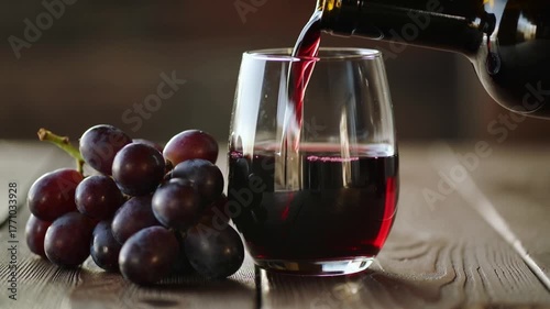 Vinous Indulgence: A pour of rich red wine streams into a clear glass, accompanied by a cluster of fresh grapes, evoking the sensory experience of a fine vintage. 