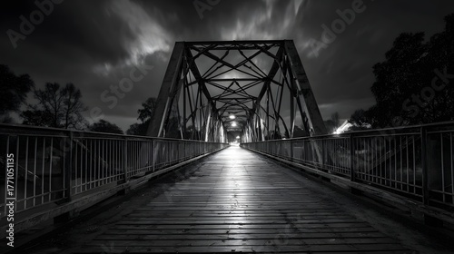 Dramatic long exposure captures a historic metal truss bridge at night with moody clouds overhead