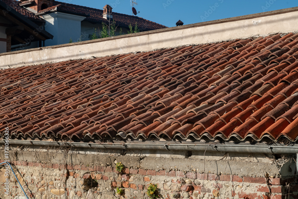 Naklejka premium Detail of a building with a pitched roof covered with elegant terracotta tiles, with well-defined upper gable lines and ridge tiles, accompanied by a functional gutter.