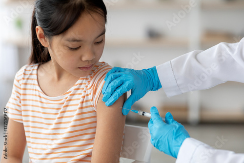 Cuadro en lienzo Medical professional in gloves is giving a vaccine to a young girl in a striped shirt at a clinic