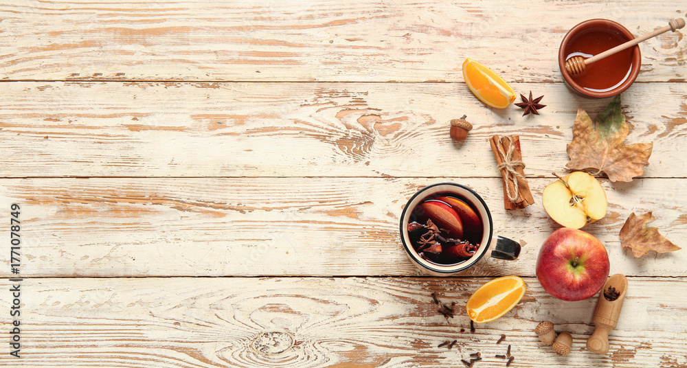 Fototapeta premium Cup of hot mulled wine with apple and orange on white wooden background