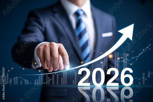 Businessman points to upward trending graph with year 2026 and abstract city background