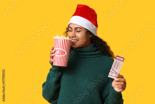 Beautiful young African-American woman in Santa hat with cinema ticket and bu...