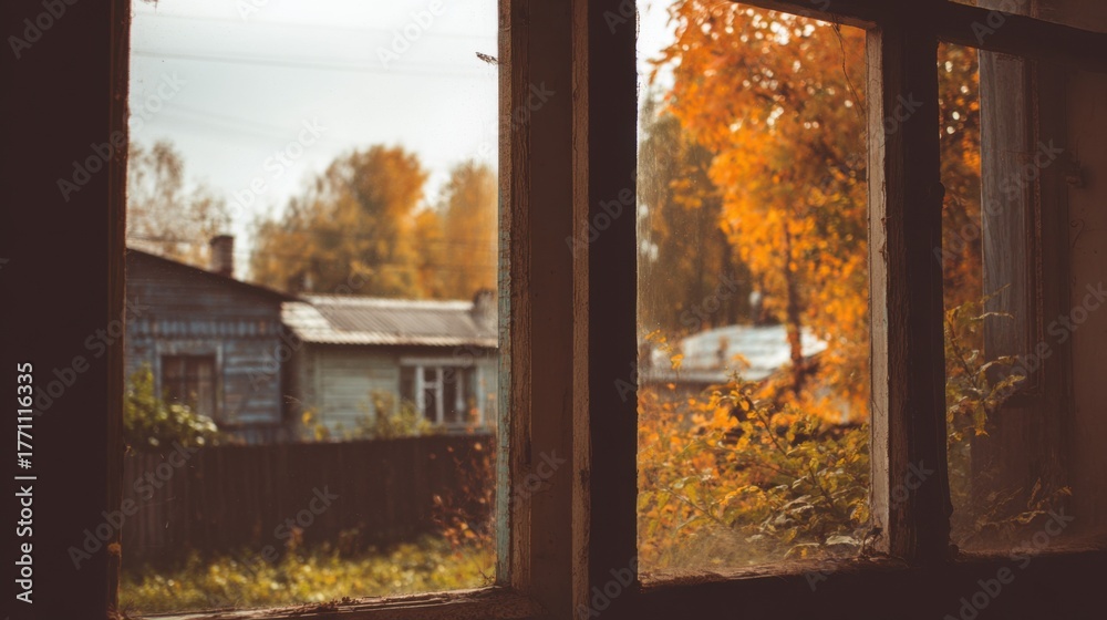 Obraz premium Autumnal Window View: A warm, nostalgic view from an aged window showcases the vivid colors of autumn foliage, with a glimpse of a rustic building in the background.
