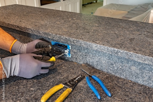 Electrician installing black GFCI outlet on granite kitchen island, Florida, USA