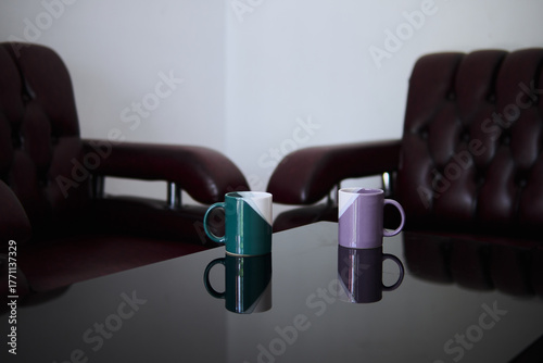 Two coffee mugs sit on a table between two chairs