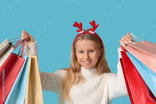 Cute girl in reindeer horns with shopping bags on blue background. Christmas ...