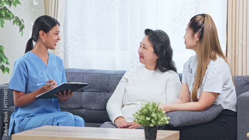 Asian Elderly woman caregiver consultation living room with nurse clipboard and supportive care compassionate home visit interview showing attentive healthcare assessment and family support during