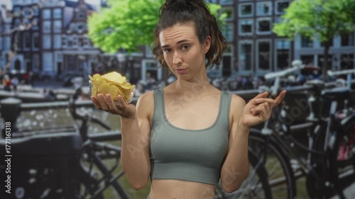 Woman pointing at a clear bowl of potato chips by a canal with a dubious look on her face; indecision choice.