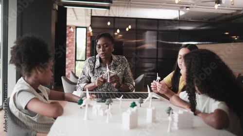 Black female teacher teaches and instructs primary girls group students, clean energy lesson at learning table in science classroom, discusses experiment knowledge for children of elementary school.