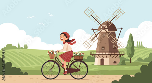Cheerful girl cycling past a windmill on a sunny day in the countryside