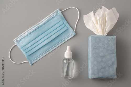Top view of a medical mask, antiseptic and a box of tissues on a gray background
