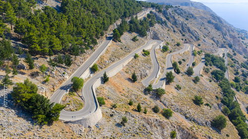 Winding mountain road with sharp 180-degree hairpin turns, surrounded by rugged landscape.