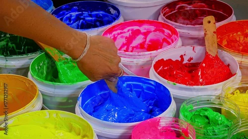 Scoop of Blue Plastisol Ink from a White Bottle for Fabric Prints. A vivid assortment of paint containers filled with bright pigments, showcasing texture, richness, and the beauty of mixed colors.