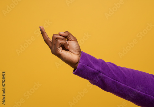 A person's hand with dark skin, extending index finger, beckoning gesture, isolated against a yellow background.