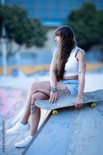 Tattooed woman relaxing at skatepark with skateboard