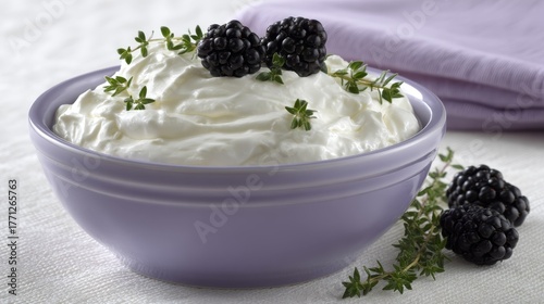 Highangle shot of creamy almond yogurt in a soft lavender bowl garnished with blackberries and fresh thyme, on a textured white background with copy space for branding or text