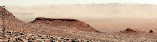 An arid, rocky, and expansive martian landscape with hazy distant peaks.