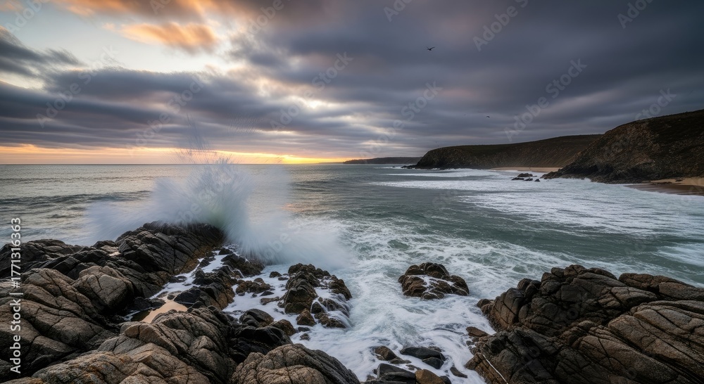 Obraz premium Ocean waves crashing against rocks under cloudy sky at sunset view