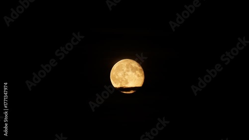 Full orange moon behind thin cloud strip at night. Close up telephoto shot, real time, no people