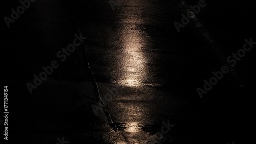 Rain fall on city street asphalt at night. Close up, telephoto footage, top down, real time, no people