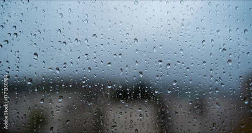 Time lapse of rain drops falling on large home window autumn day. Wide angle close up view, shallow depth of field, blurry clouds and architecture in the background, no people