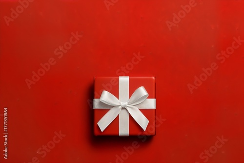 Minimalist Christmas composition with red gift box and white satin ribbon on matching red background, elegant holiday aesthetic