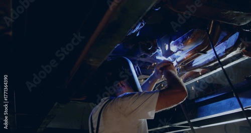 Plakat Welding technician wearing helmet welding overhead beams with torch at metal shop, sparks flying