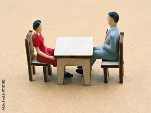 Miniature figures of a man and woman sitting at a table, having a conversation in a neutral setting