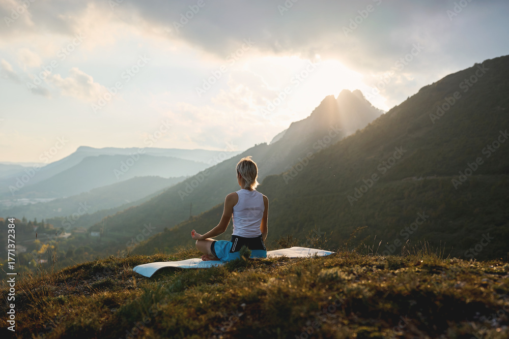 Fototapeta premium Woman meditating on mountain at sunrise with sunlight rays