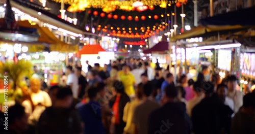 Slow motion defocused view of people crowd at night street market of Kuala Lumpur. Visitors walk along stalls of street food and snacks and affordable restaurants at famous food street at downtown