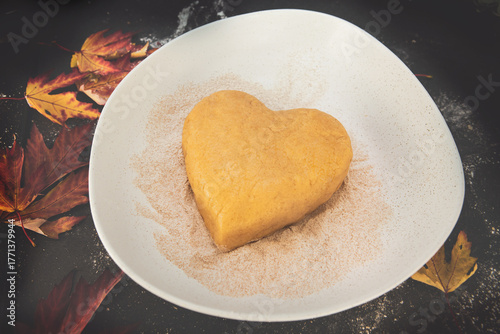 Heart-shaped shortcrust pastry on a floured dark surface, surrounded by autumn maple leaves — cozy seasonal baking and fall-inspired homemade cookie preparation moment.