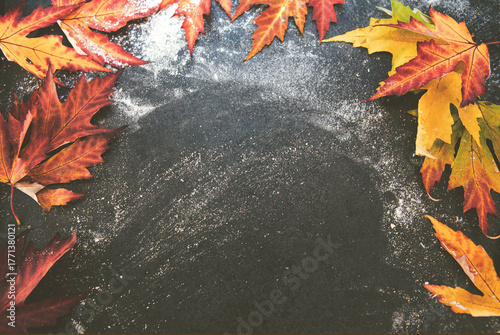 Top view of a dark floured surface framed with colorful autumn leaves, creating a rustic background and blank space for seasonal recipe text or fall baking presentation.