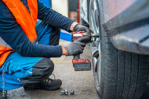 Mechanic using an impact wrench to remove lug nuts from a car wheel. Seasonal tire change and professional car service in preparation for winter.