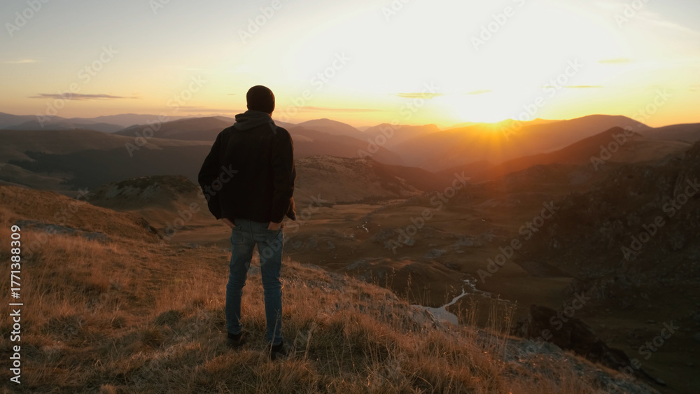 Fototapeta premium Man standing on a mountain ridge watching the sunset over the valley on a clear evening
