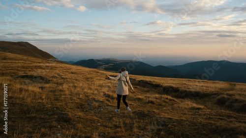 Woman enjoying the open landscape with mountains and clouds at sunset, embracing nature and freedom, feeling serene and connected to the environment