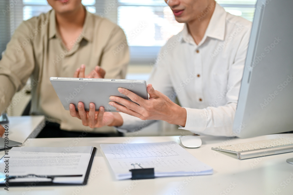 Obraz premium Close up of businessman talking and coworker holding showing a tablet at table in company's office.