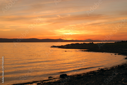Beautiful atmospheric sunset with warm orange and pink hues, illuminating the sky and landscape in soft glowing light.