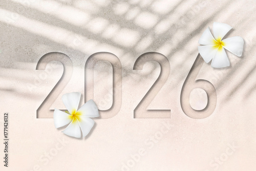 Happy New Year 2026 greeting card, Flat lay or top view of number 2026 debossing on white sand beach texture with shadows of palm leaf and white Plumeria flowers. New Years concept.