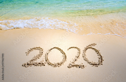 Happy New Year 2026, lettering on the beach with wave and clear blue sea. Numbers 2026 year on the sea shore, message handwritten in the golden sand on beautiful beach background. New Year concept.