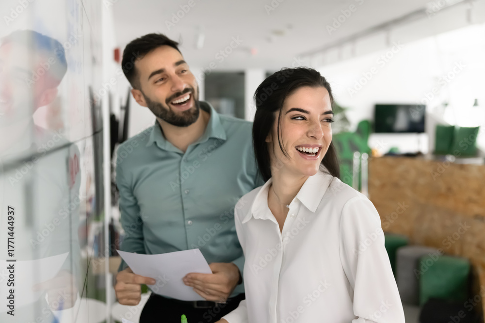 Obraz premium Overjoyed millennial man woman coworkers laughing near visual schedule board