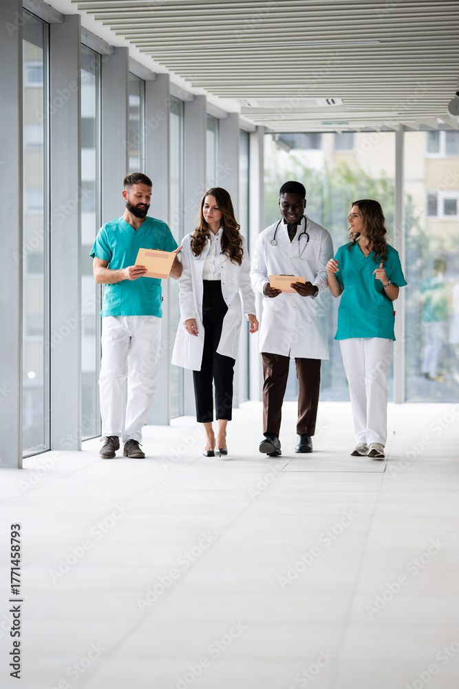 Fototapeta premium Diverse medical team walking hospital hallway discussing patient records