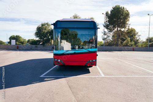 Modern red electric bus standing in a sunny empty parking lot, representing sustainable public transport and urban mobility