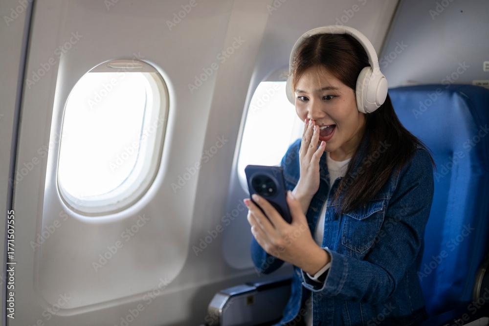 Fototapeta premium Woman experiencing excitement using smartphone on airplane flight