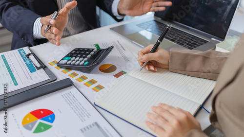 Business colleagues are engaged in a financial meeting, reviewing colorful charts and reports. They exchange ideas, make notes, and analyze strategies to achieve effective results.