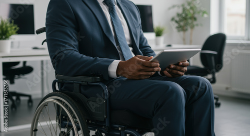Professional businessman in a wheelchair using a digital tablet in a modern office environment, focusing on inclusive workplace innovation