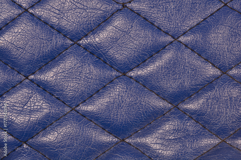 Obraz premium A detailed close-up of a luxurious deep blue, textured faux leather surface with a distinct diamond-shaped quilted stitching pattern, ideal for a background.