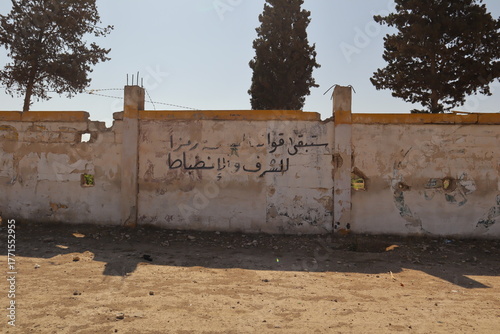War damaged wall at the Military Infantry School in Aleppo, Syria, with Arabic graffiti saying “Our armed forces will remain a symbol of honor and discipline.” Once contested, now under Syrian control